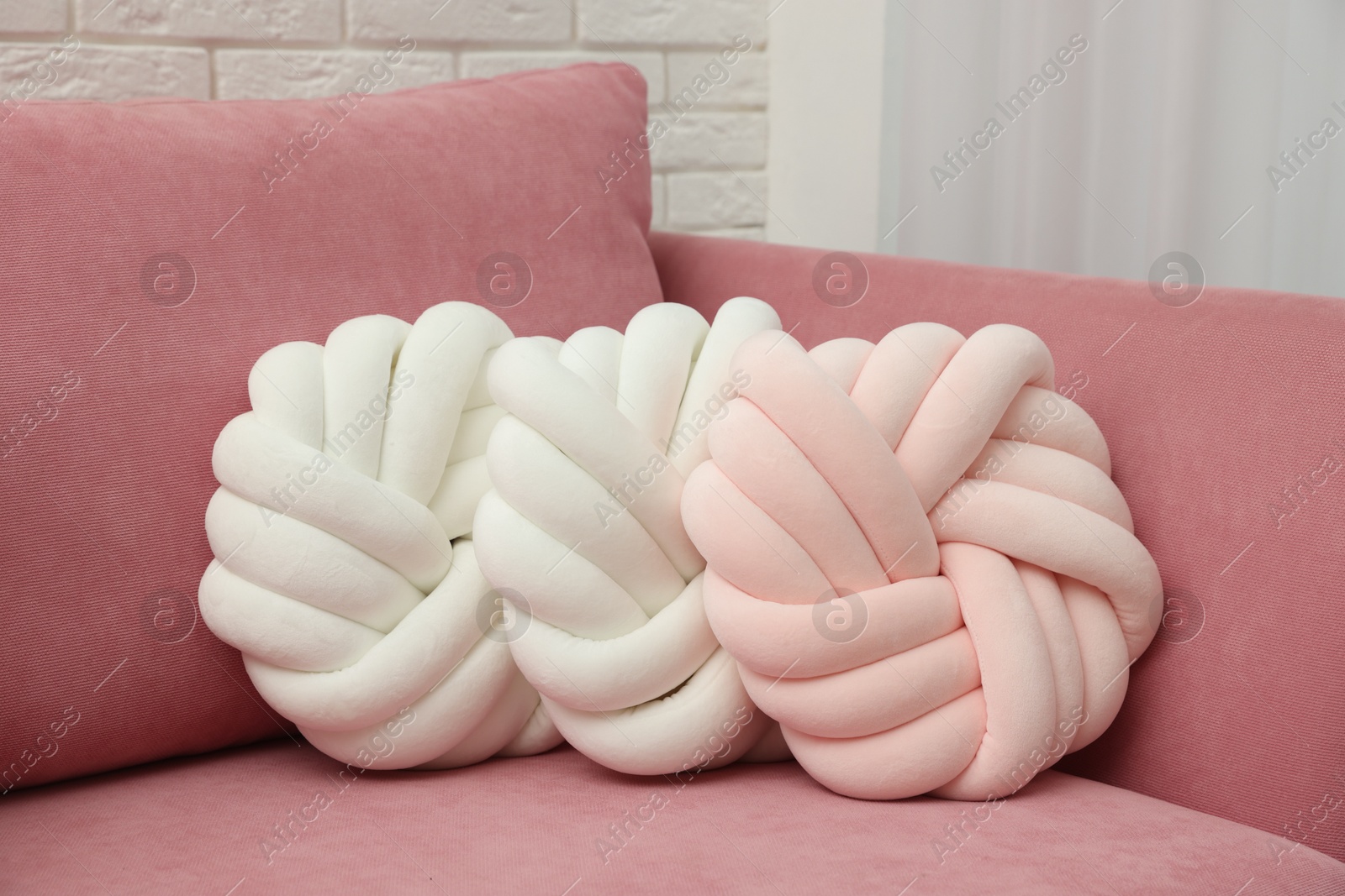 Photo of Three decorative pillows on pink sofa indoors