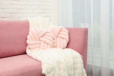 Decorative pillows and fluffy blanket on pink sofa indoors