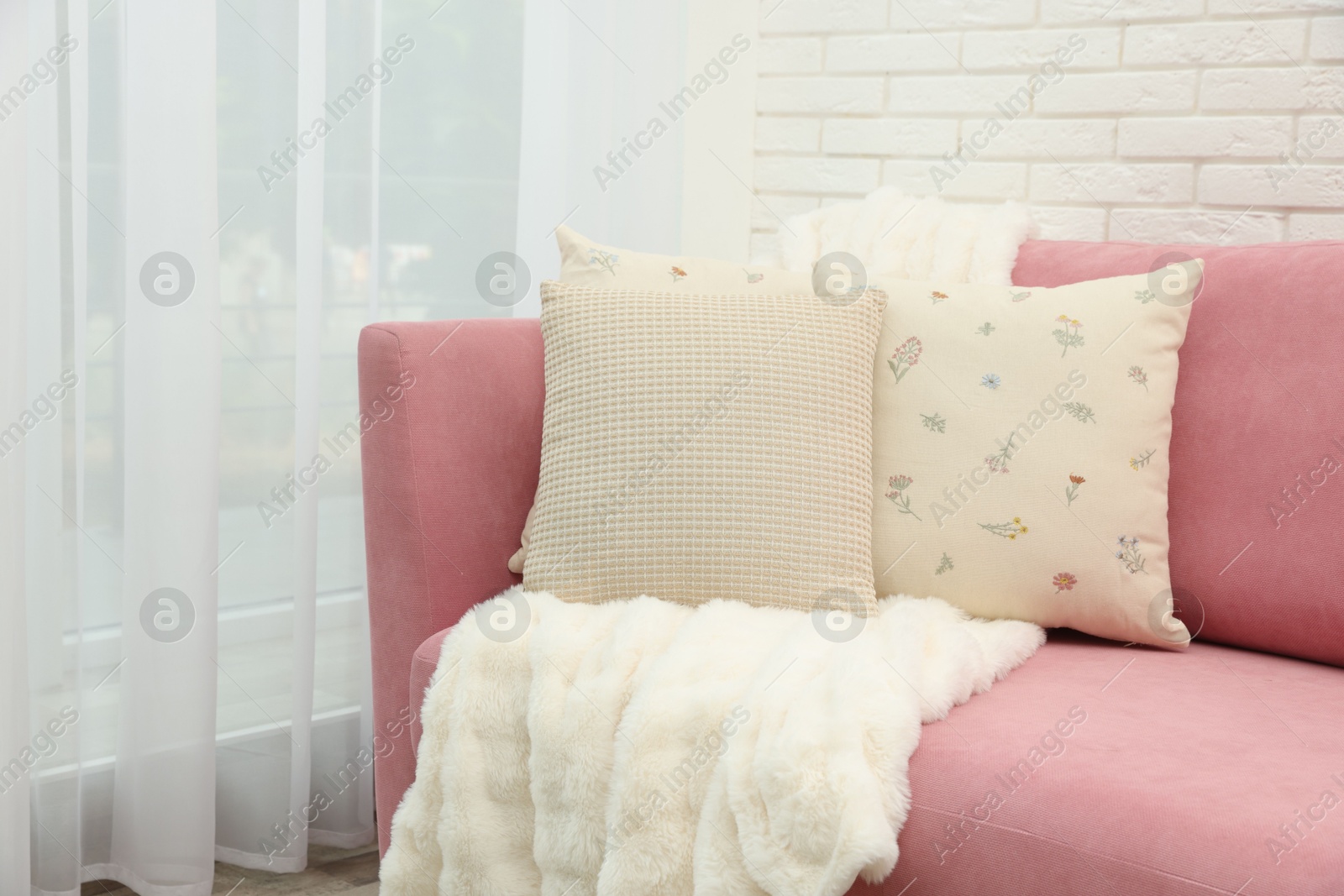 Photo of Decorative pillows and fluffy blanket on pink sofa indoors