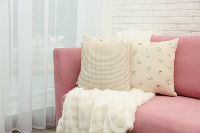 Photo of Decorative pillows and fluffy blanket on pink sofa indoors