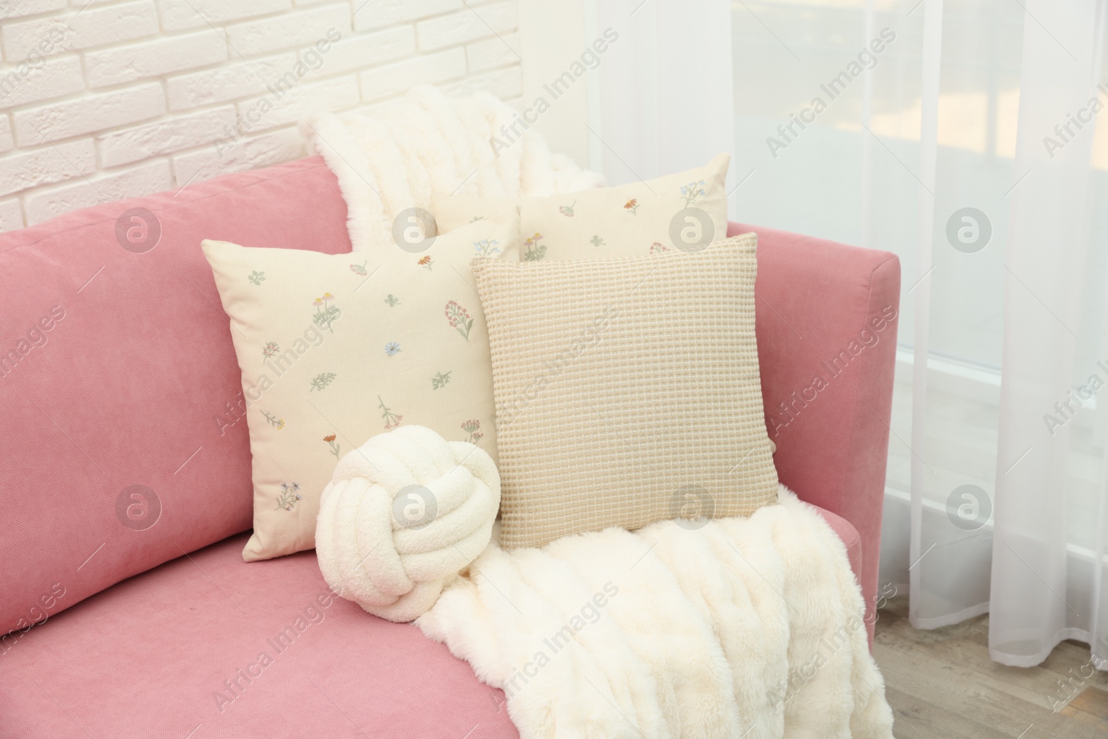 Photo of Decorative pillows and fluffy blanket on pink sofa indoors