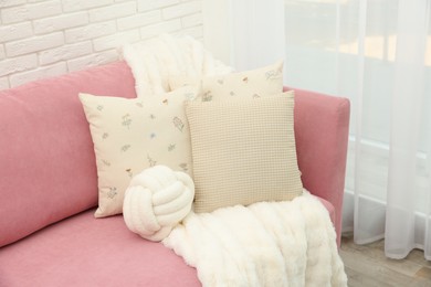 Decorative pillows and fluffy blanket on pink sofa indoors