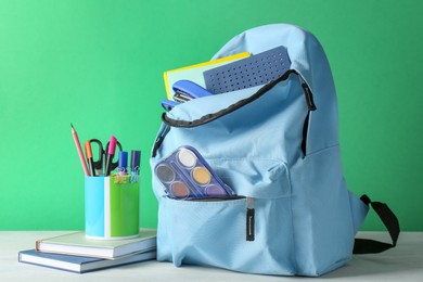 Backpack with different school stationery on white table against green background