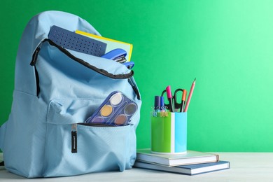 Photo of Backpack with different school stationery on white table against green background