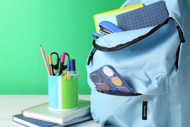 Photo of Backpack with different school stationery on white table against green background