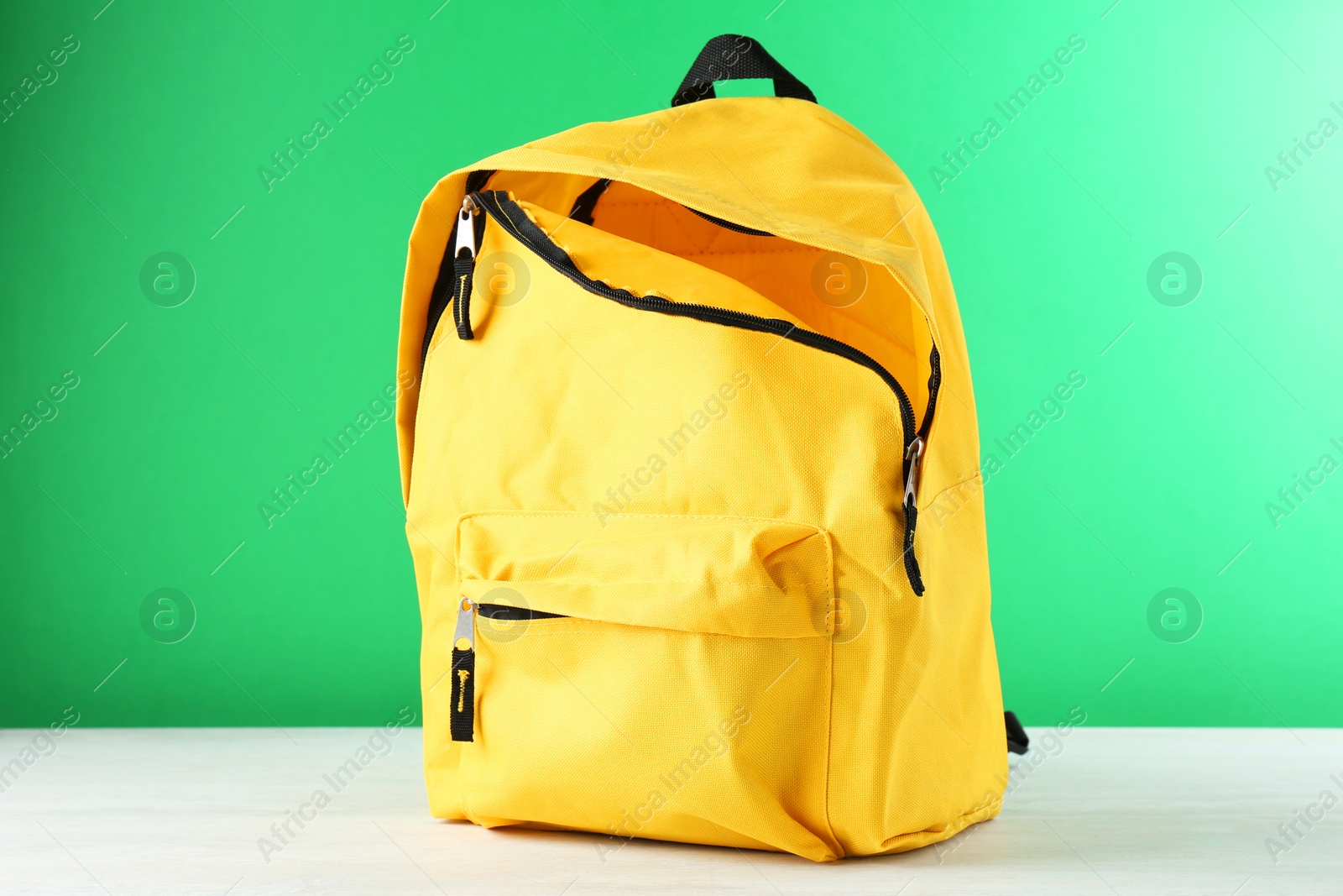 Photo of One yellow backpack on white table against green background