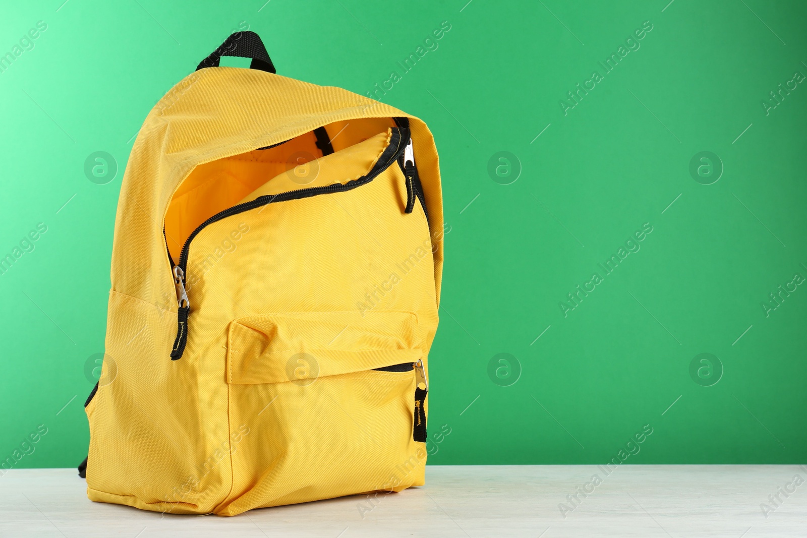 Photo of One yellow backpack on white table against green background, space for text