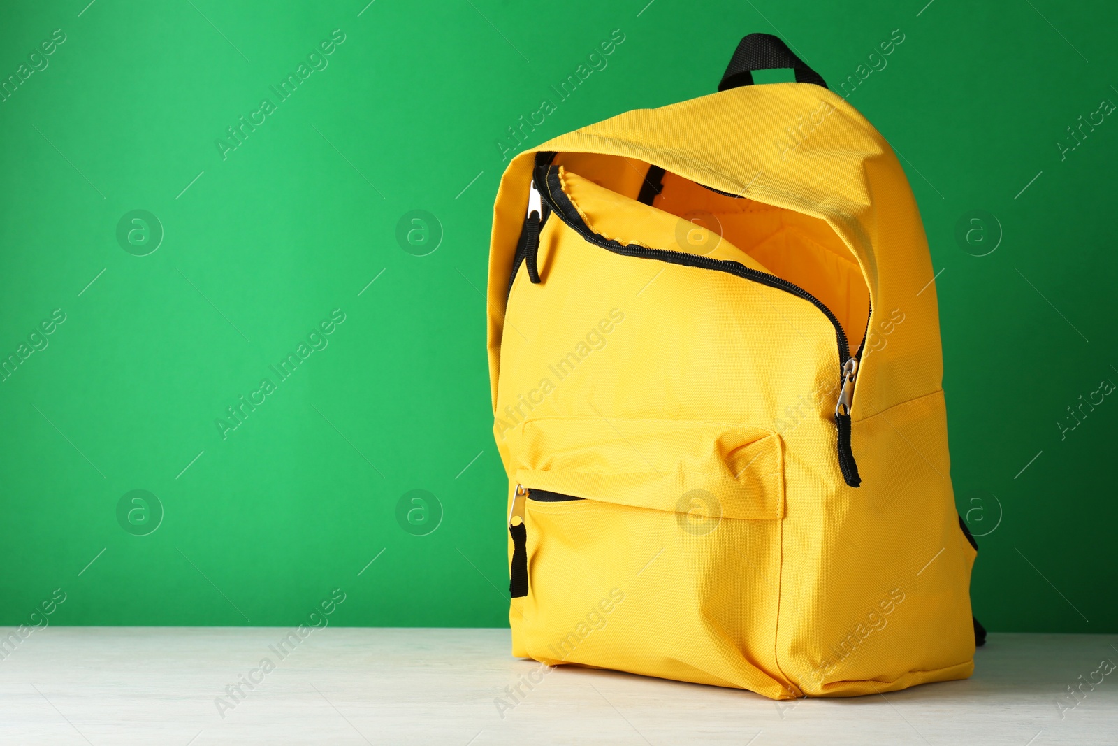 Photo of One yellow backpack on white table against green background, space for text