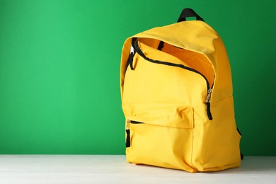 Photo of One yellow backpack on white table against green background, space for text