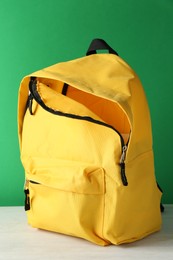 Photo of One yellow backpack on white table against green background