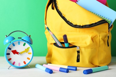 Photo of Backpack with different school stationery and alarm clock on white table against green background