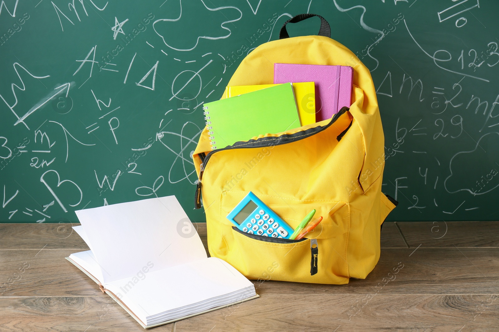 Photo of Backpack with different school stationery on wooden table against green chalkboard