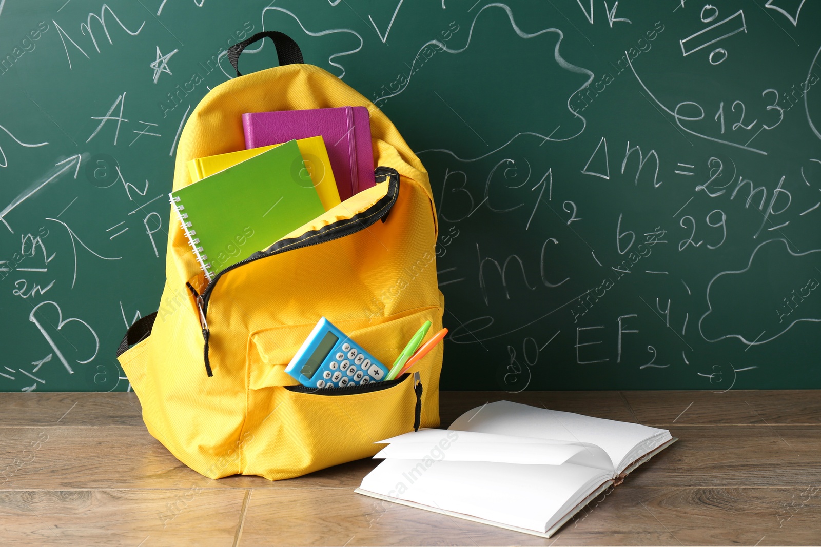 Photo of Backpack with different school stationery on wooden table against green chalkboard