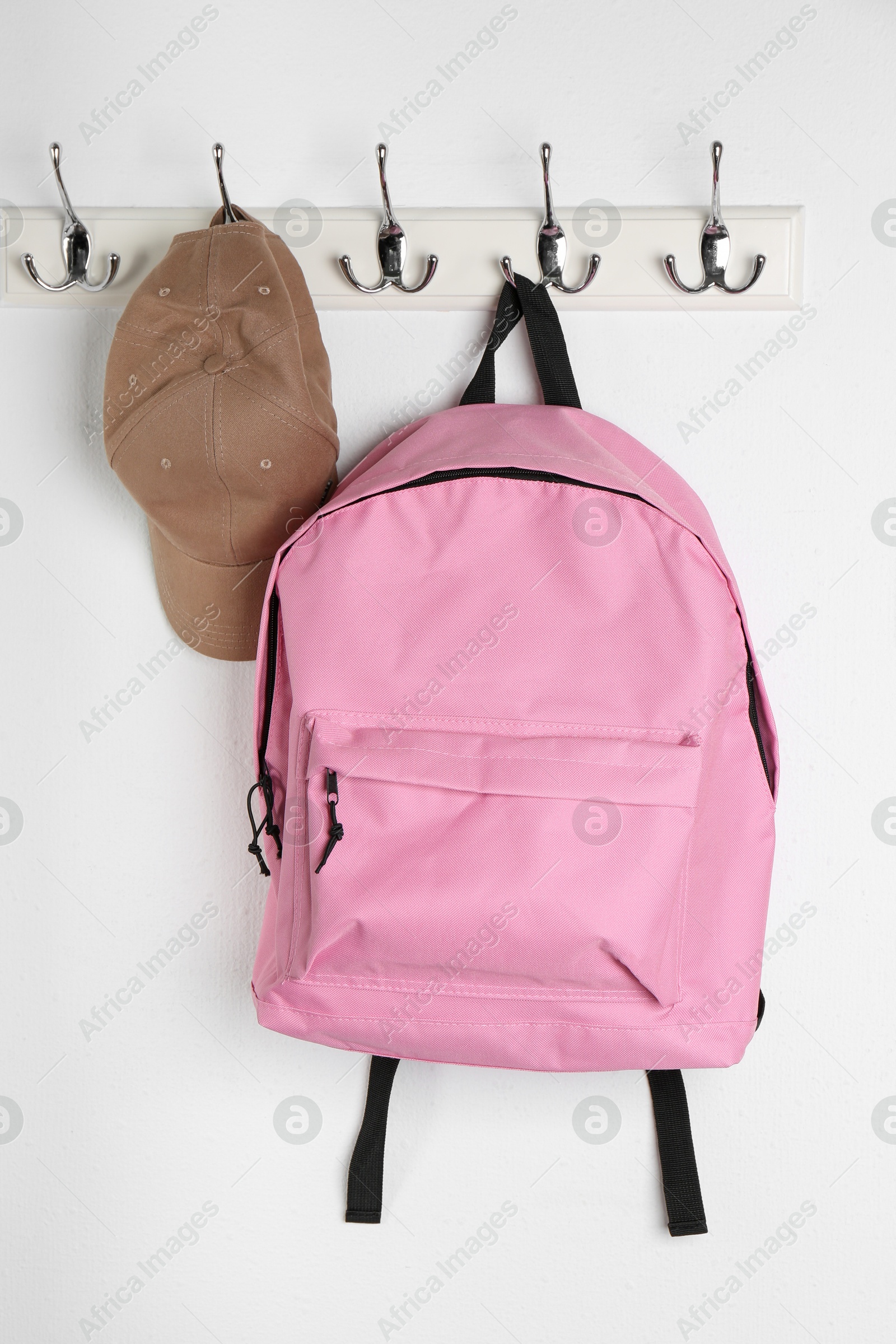 Photo of Pink backpack and cap hanging on white wall