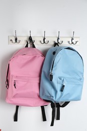 Photo of Bright backpacks hanging on white wall. Back to school