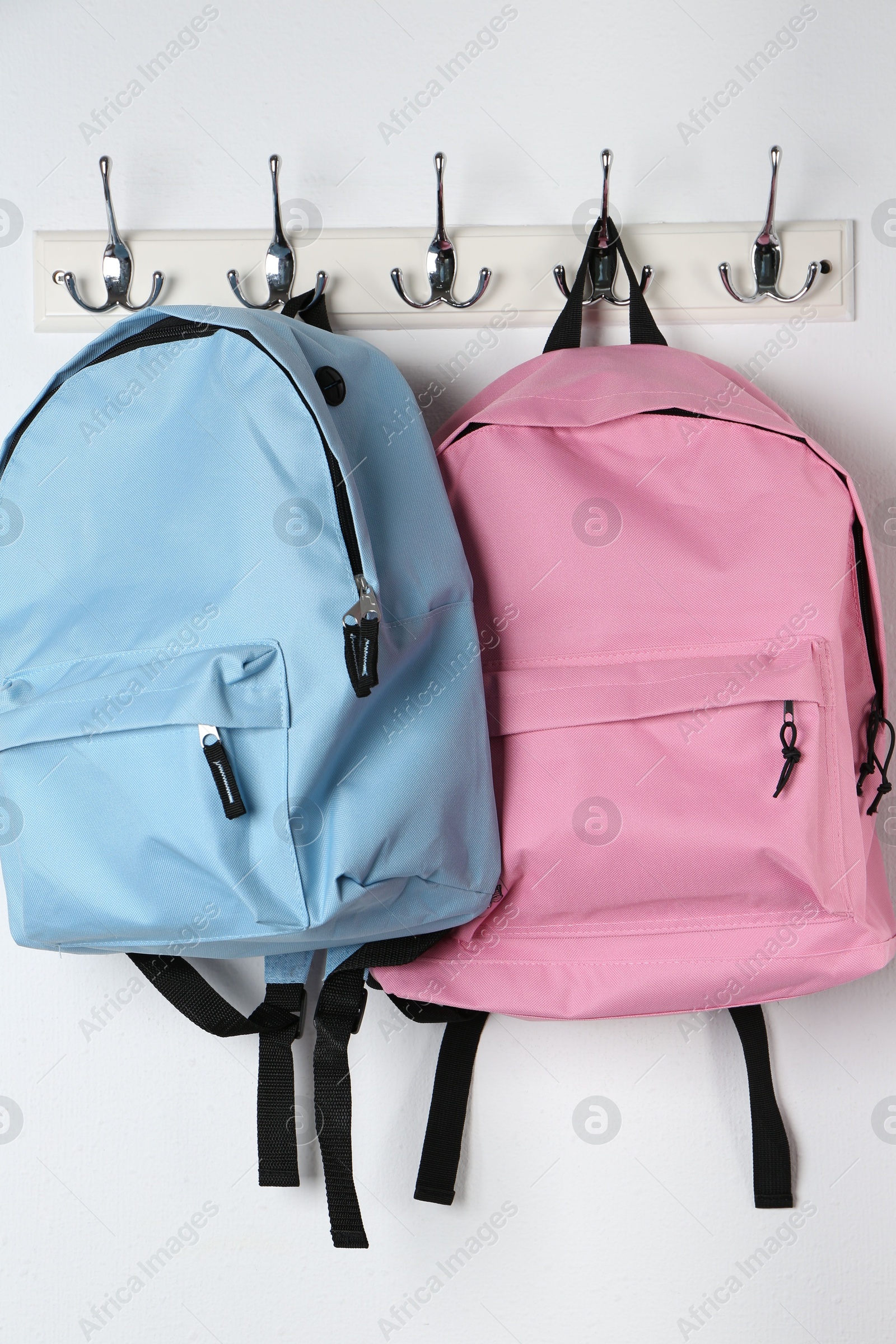 Photo of Bright backpacks hanging on white wall. Back to school