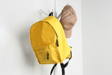 Photo of Yellow backpack and cap hanging on white wall