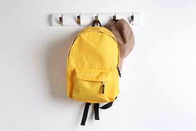 Photo of Yellow backpack and cap hanging on white wall