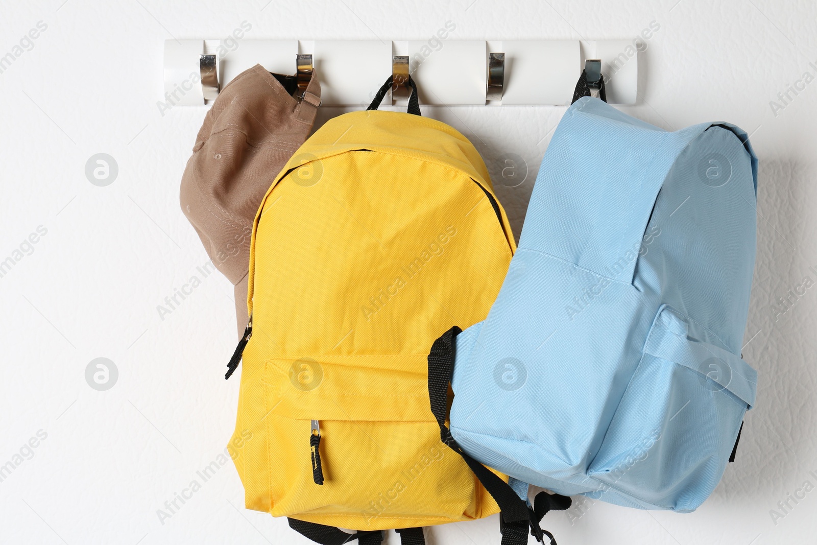 Photo of Bright backpacks and cap hanging on white wall