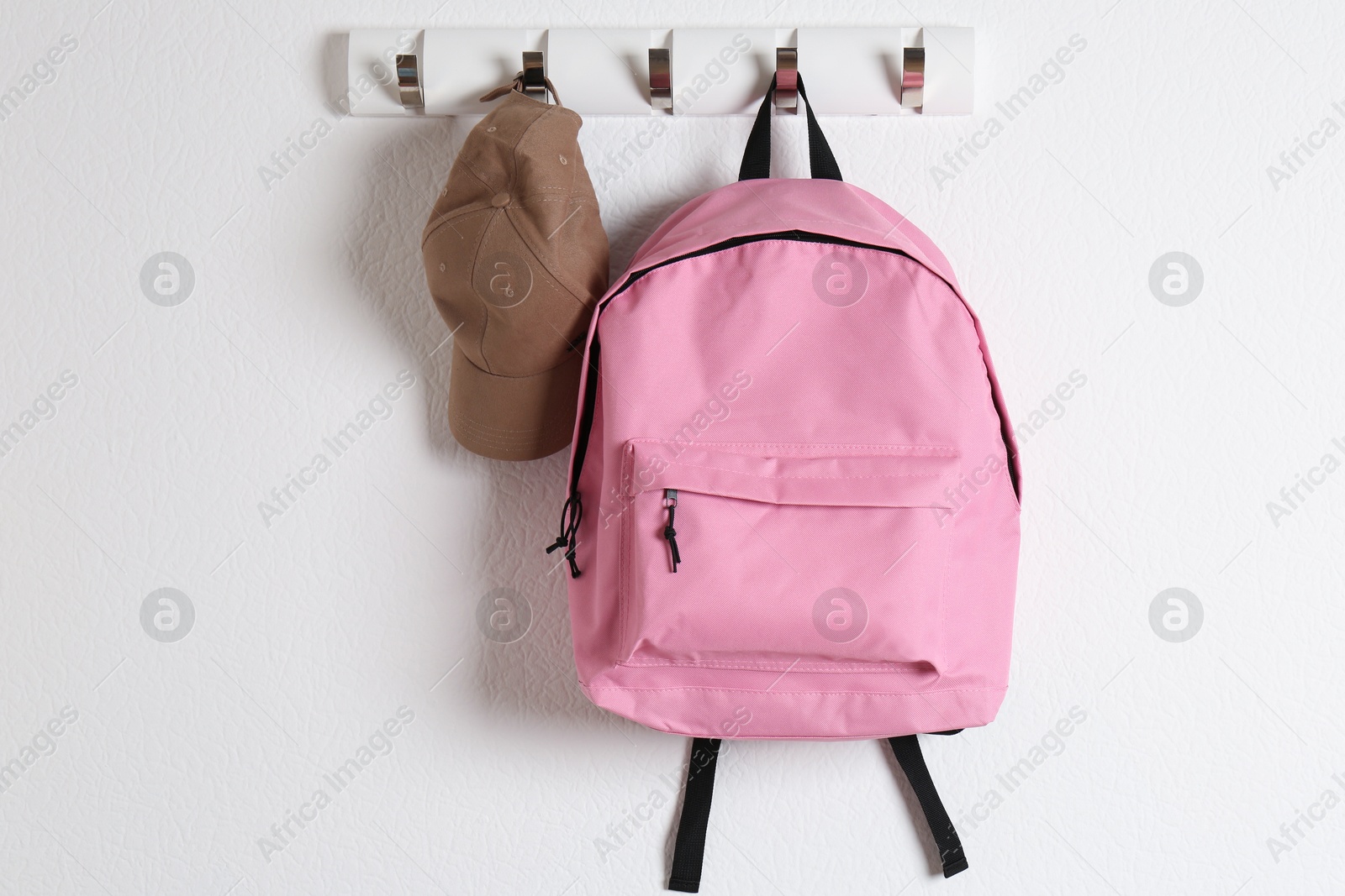 Photo of Pink backpack and cap hanging on white wall