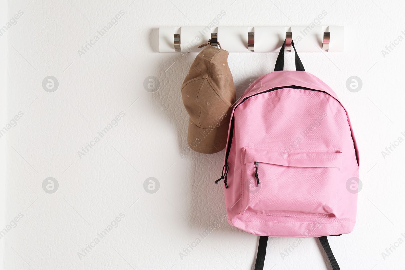 Photo of Pink backpack and cap hanging on white wall, space for text