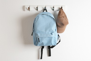 Photo of Light blue backpack and cap hanging on white wall