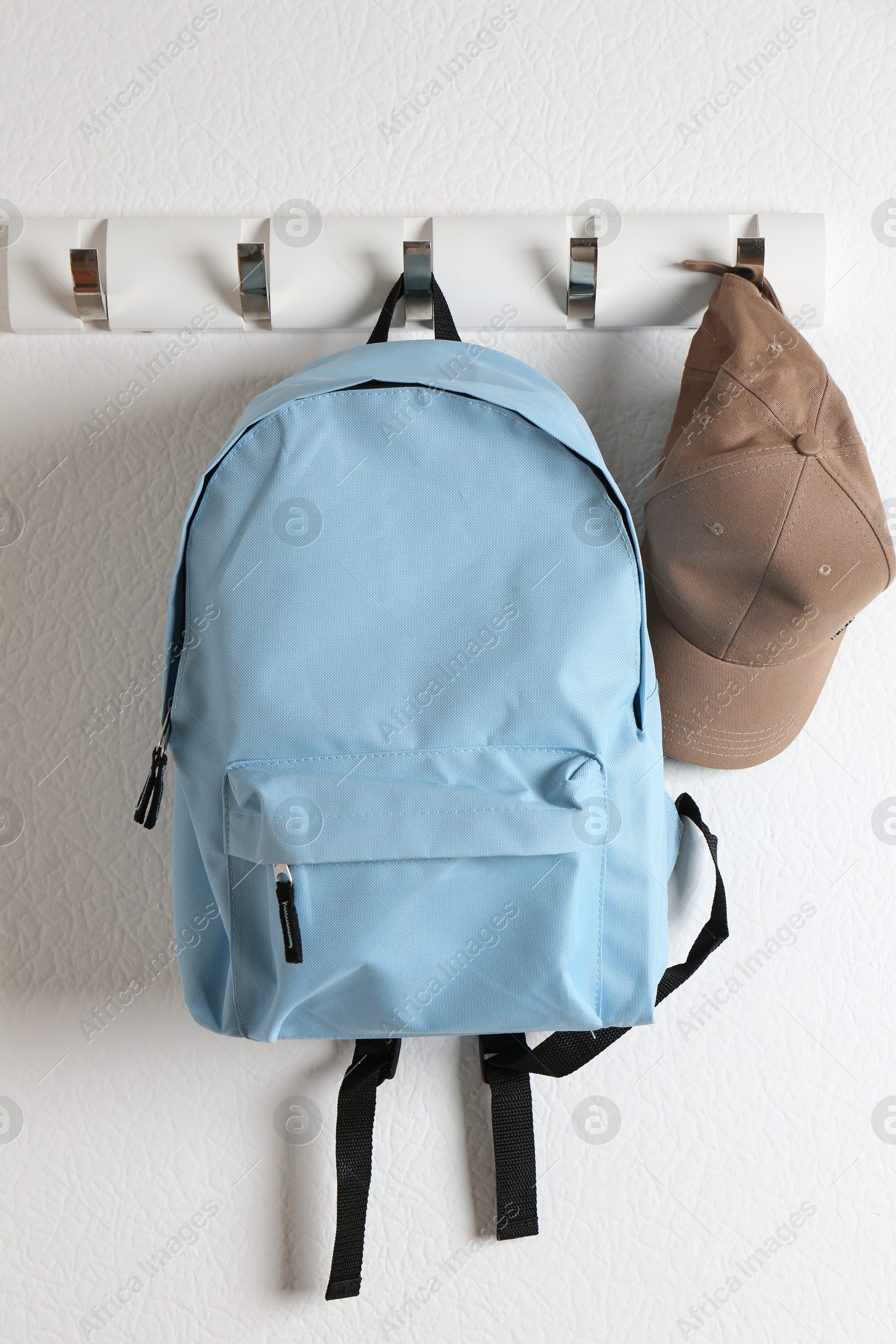 Photo of Light blue backpack and cap hanging on white wall