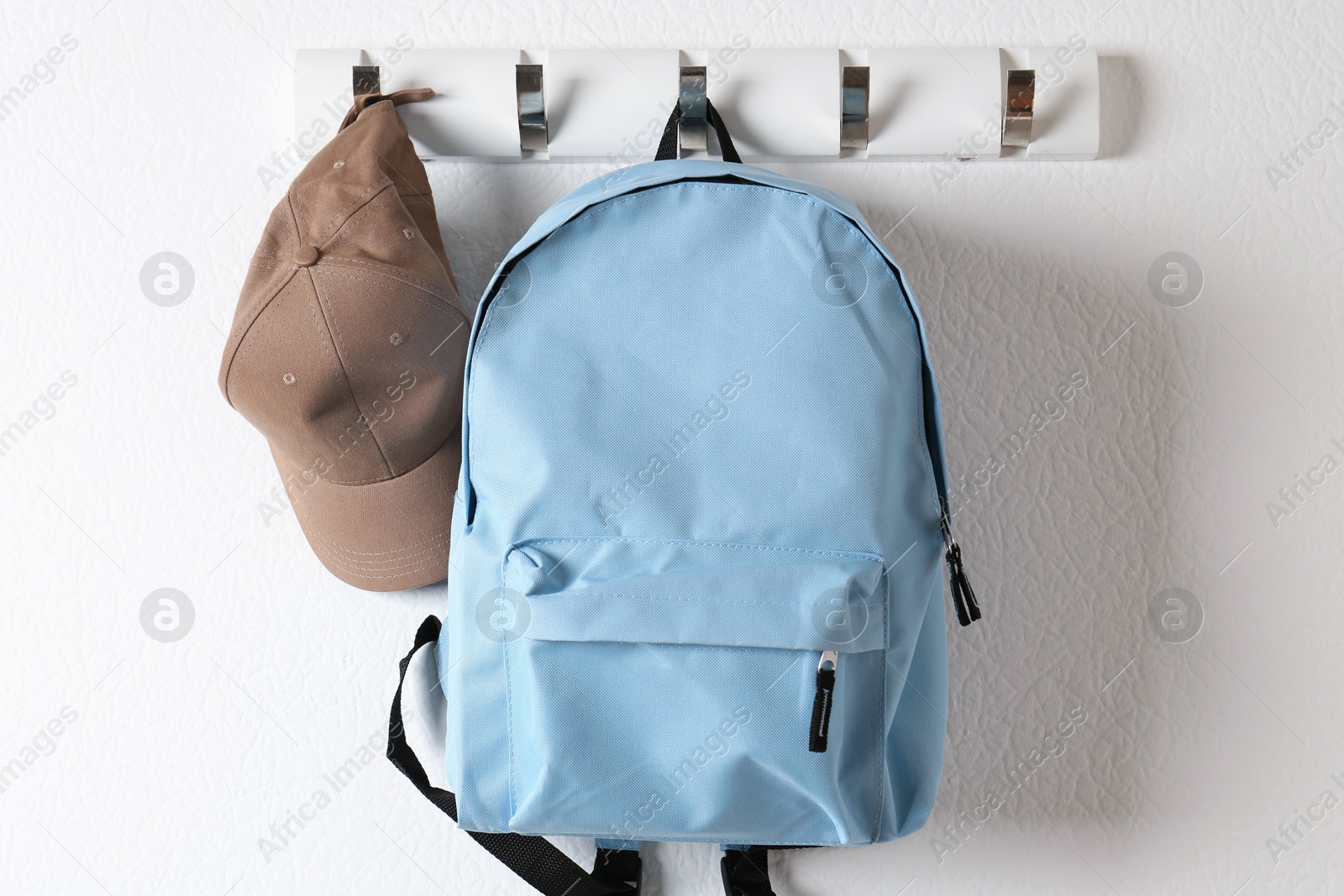 Photo of Light blue backpack and cap hanging on white wall