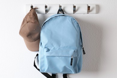 Light blue backpack and cap hanging on white wall