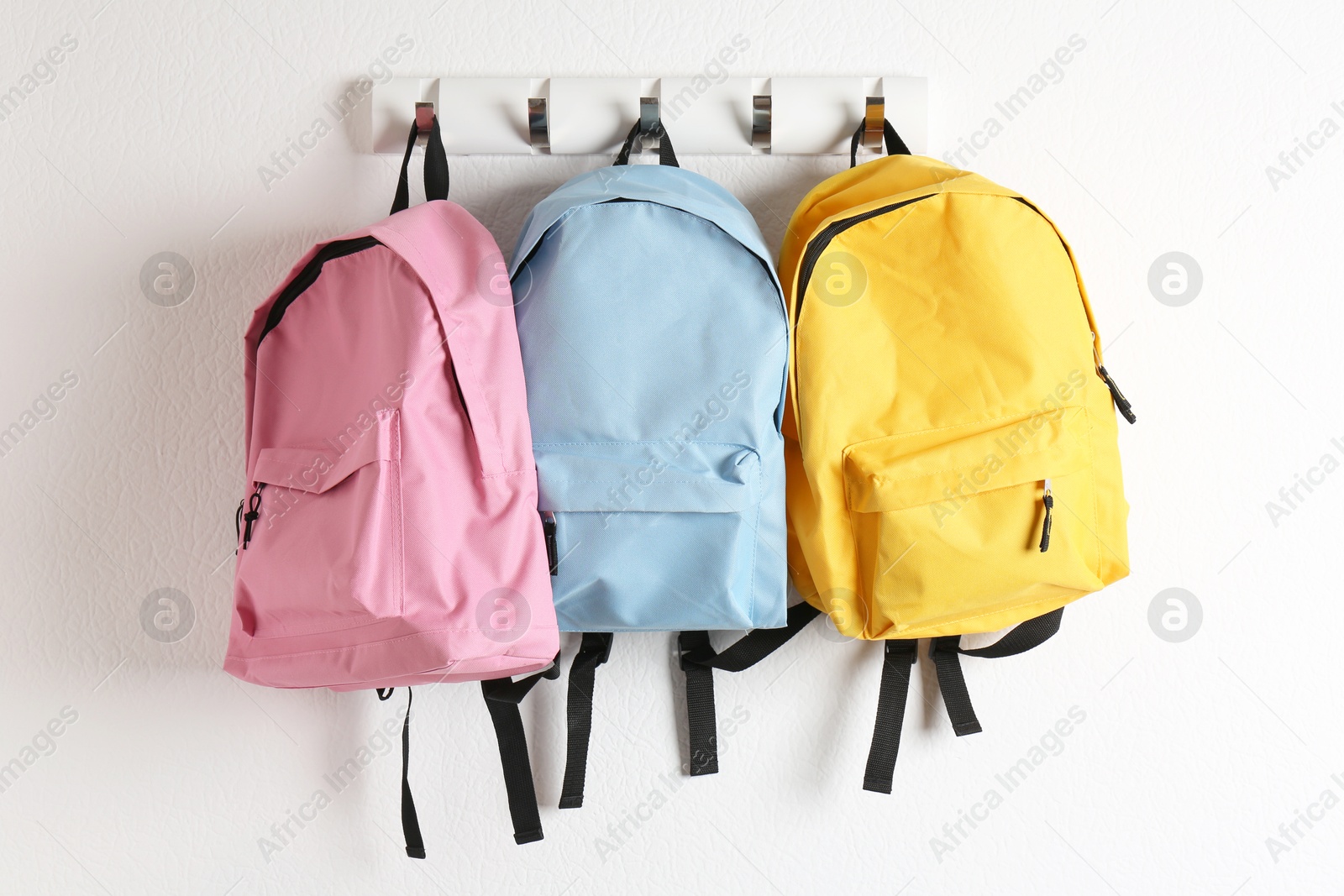 Photo of Bright backpacks hanging on white wall. Back to school