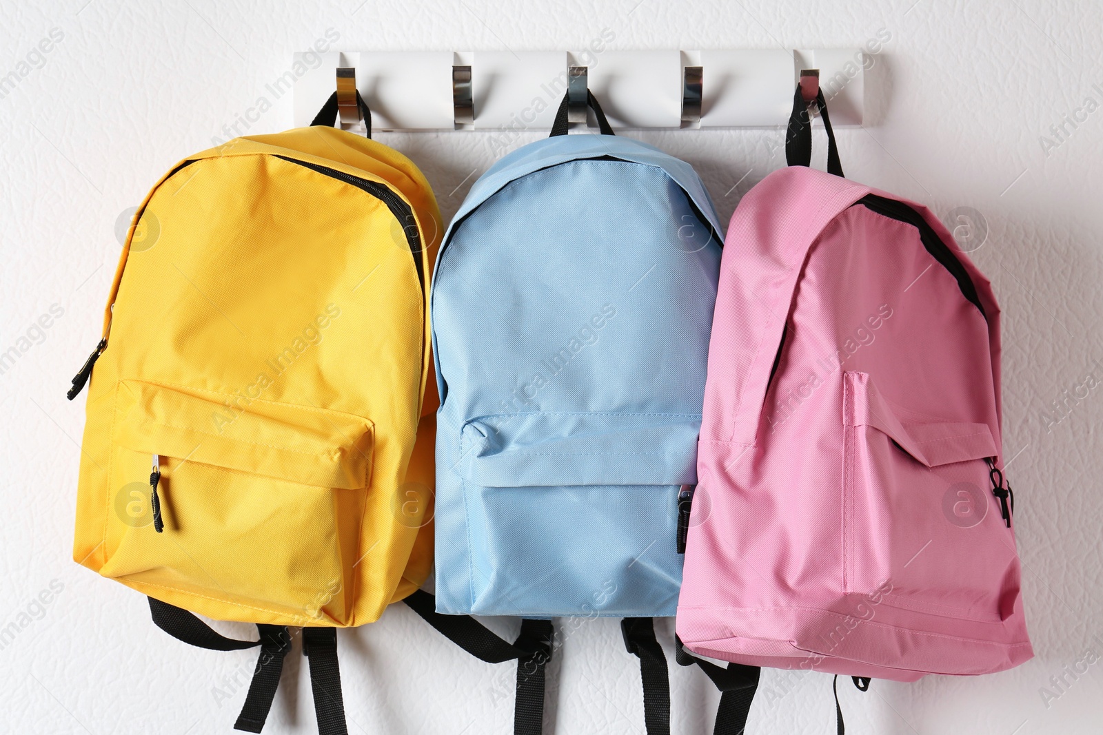 Photo of Bright backpacks hanging on white wall. Back to school