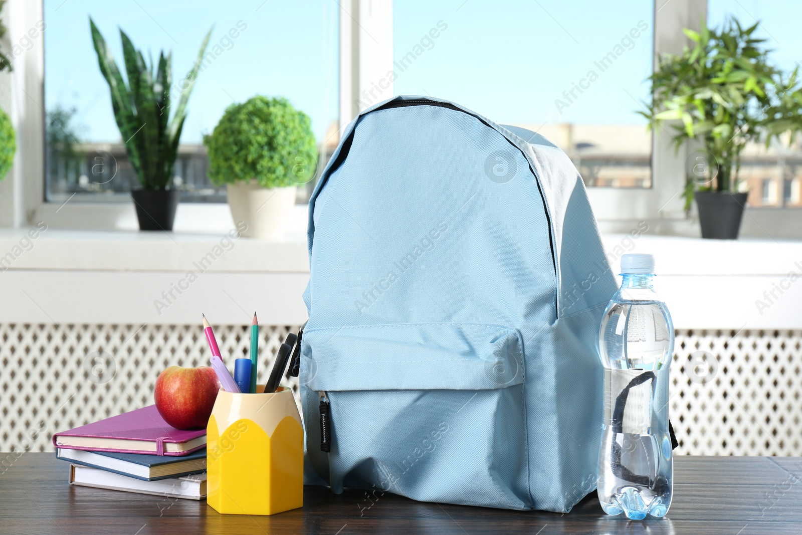 Photo of Backpack with different school stationery, apple and bottle of water on wooden table indoors