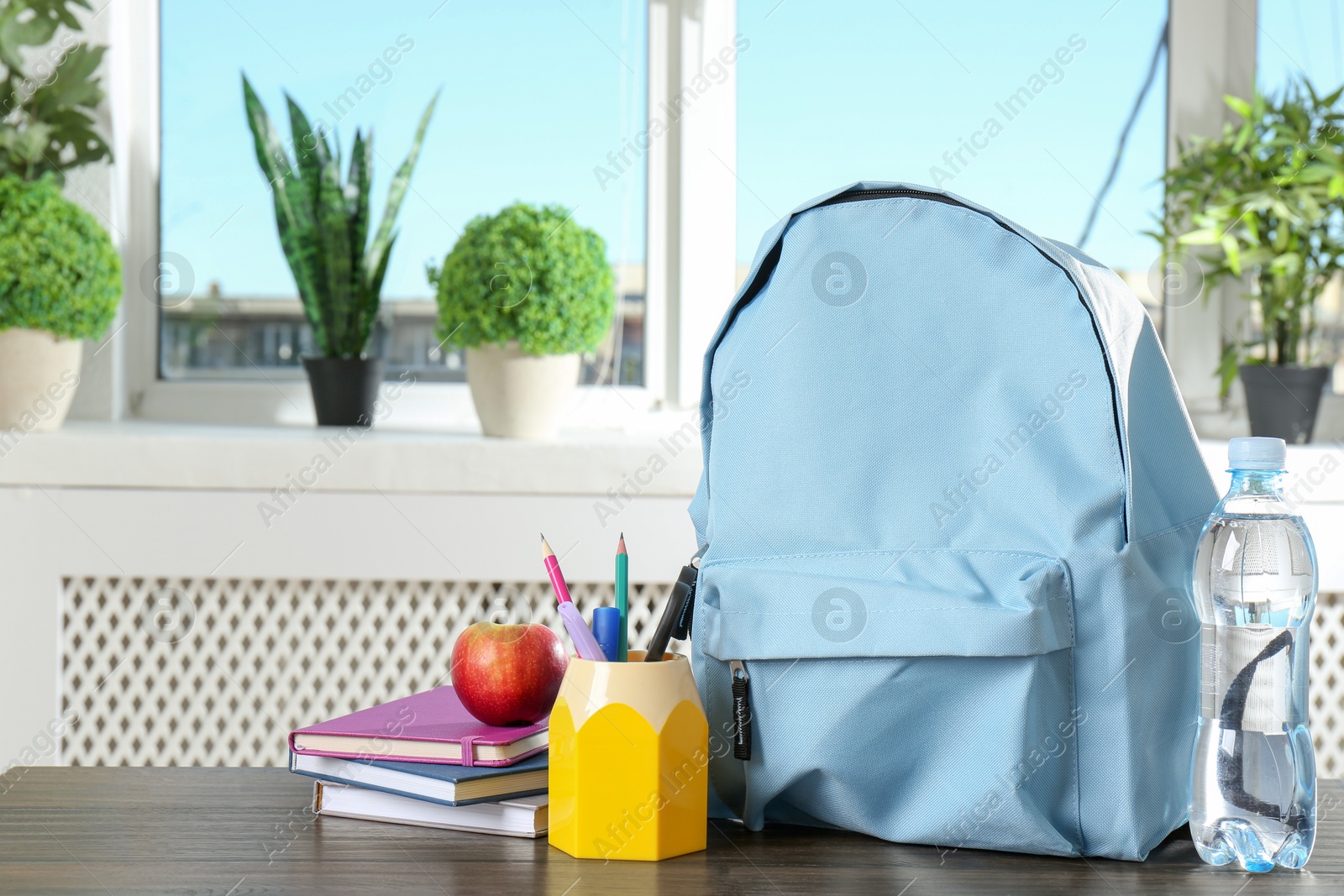 Photo of Backpack with different school stationery, apple and bottle of water on wooden table indoors