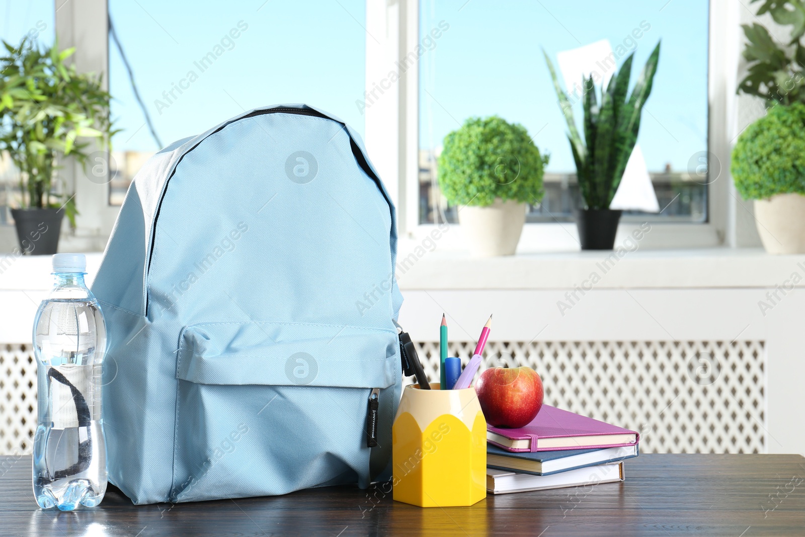 Photo of Backpack with different school stationery, apple and bottle of water on wooden table indoors