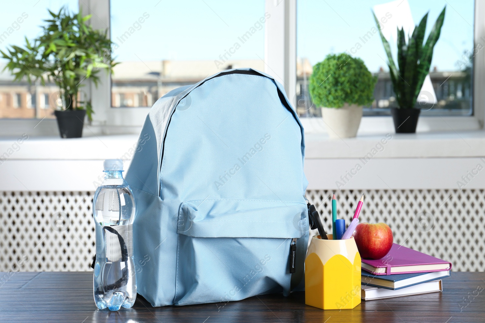 Photo of Backpack with different school stationery, apple and bottle of water on wooden table indoors