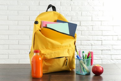 Photo of Backpack with different school stationery, apple and juice on wooden table against brick wall