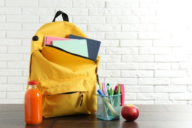 Photo of Backpack with different school stationery, apple and juice on wooden table against brick wall