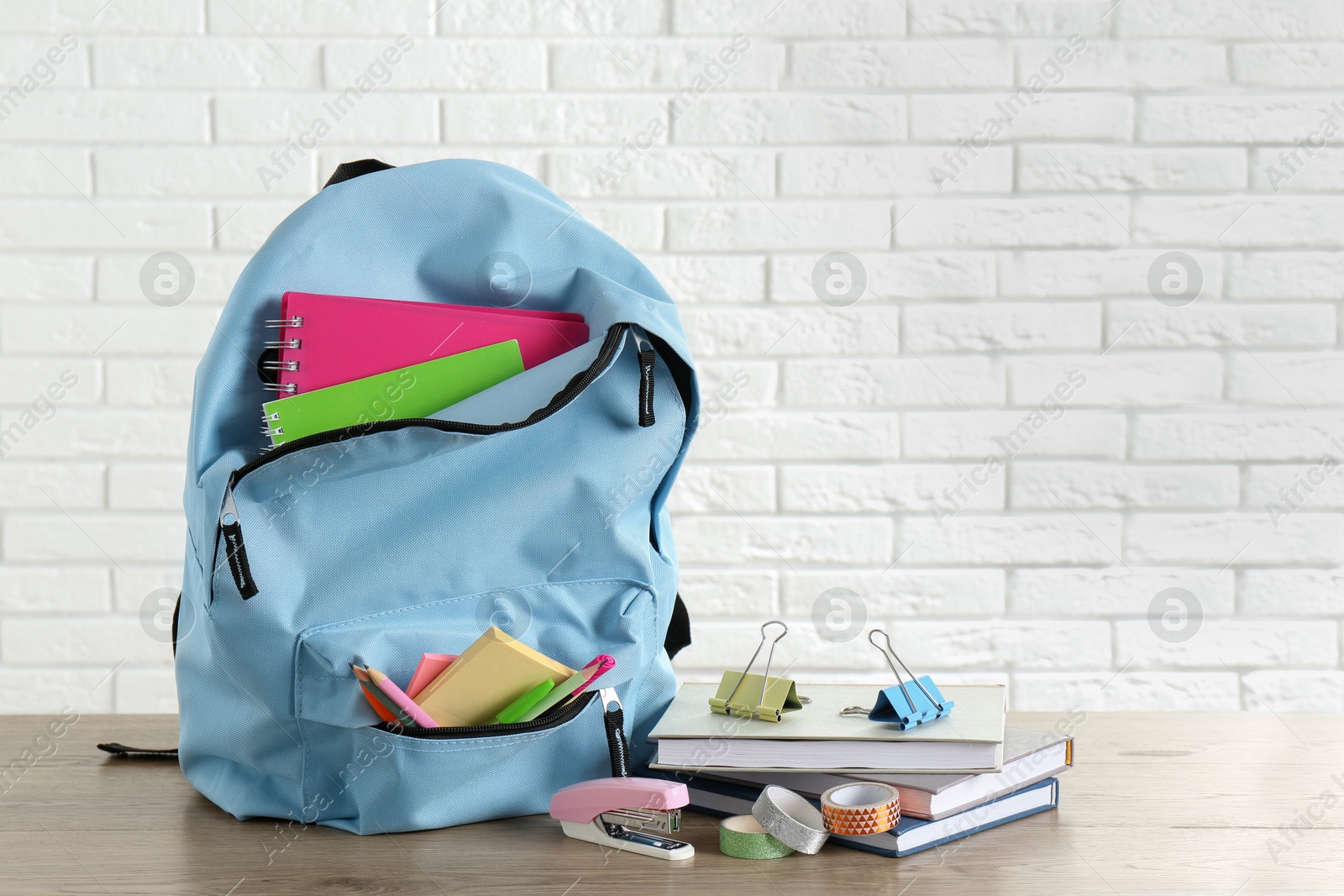 Photo of Backpack with different school stationery on wooden table against brick wall