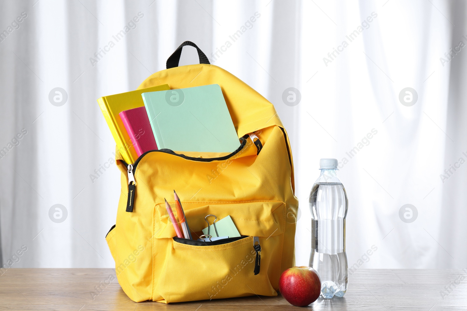 Photo of Backpack with different school stationery, bottle of water and apple on wooden table