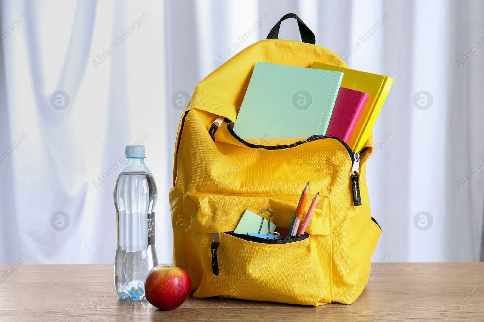 Photo of Backpack with different school stationery, bottle of water and apple on wooden table