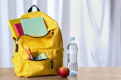 Photo of Backpack with different school stationery, bottle of water and apple on wooden table