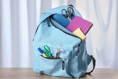 Backpack with different school stationery on wooden table