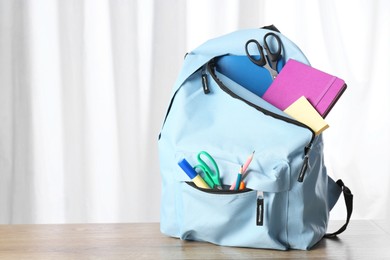 Backpack with different school stationery on wooden table