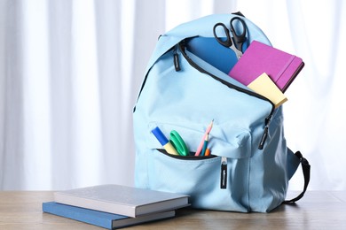 Backpack with different school stationery on wooden table