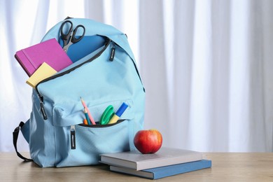 Photo of Backpack with different school stationery and apple y on wooden table