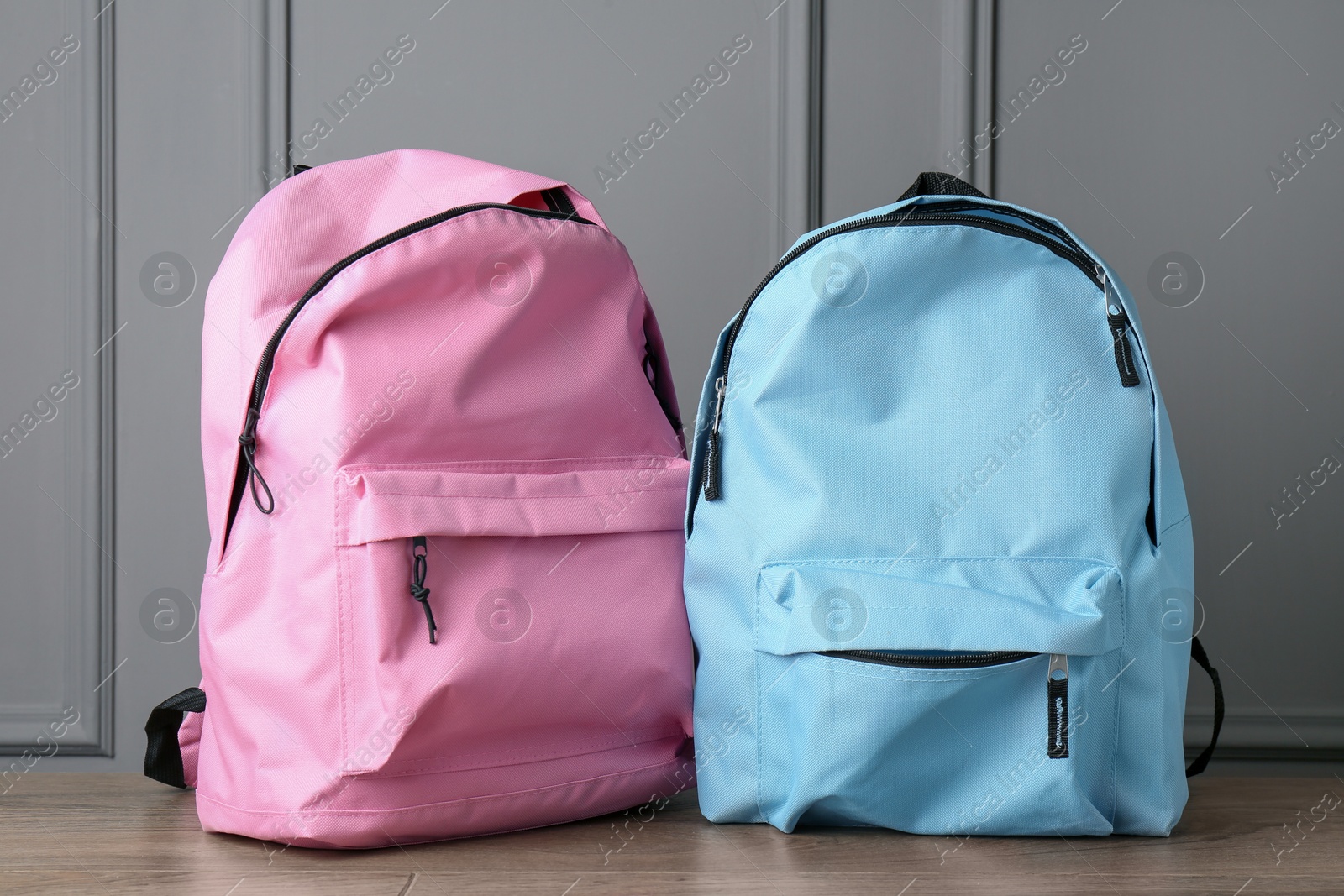 Photo of Bright backpacks on wooden table near grey wall