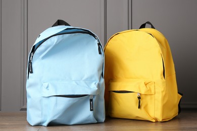 Bright backpacks on wooden table near grey wall