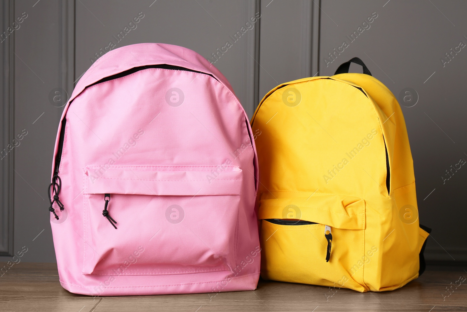 Photo of Bright backpacks on wooden table near grey wall