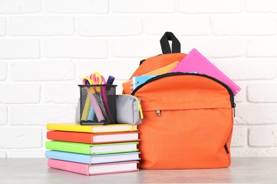 Photo of Backpack with different school stationery on light grey table near brick wall