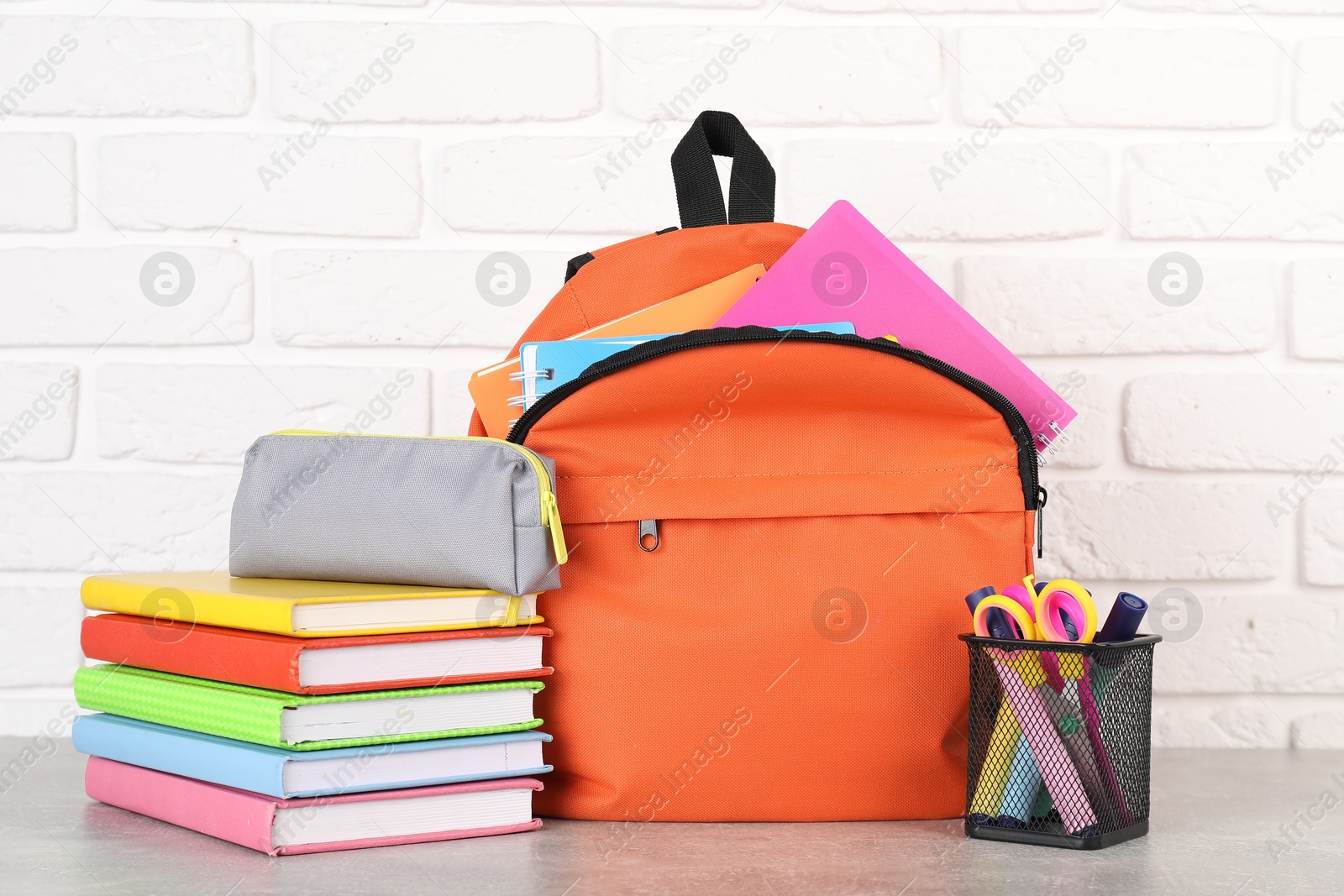 Photo of Backpack with different school stationery on light grey table near brick wall